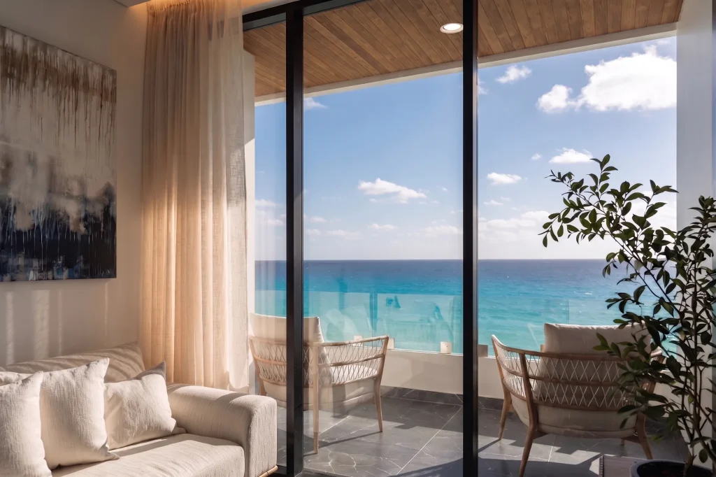 Sliding glass doors frame a private terrace with rattan armchairs above the Caribbean at Puerto Morelos